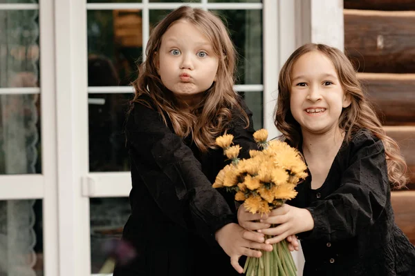 Duas Meninas Vestidos Pretos Segurar Flores Suas Mãos Sorrir Para — Fotografia de Stock