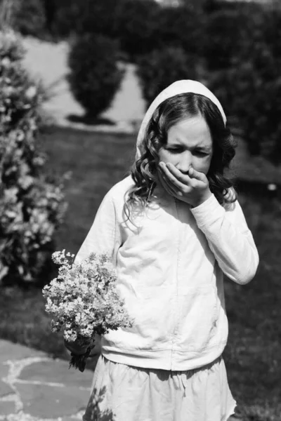 一个小女孩打喷嚏是因为她对花和花粉过敏 背景是卷曲的黑发 无忧无虑的童年花园的概念 — 图库照片