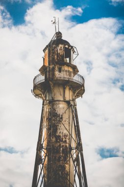 Arka plan mavi bir gökyüzü ve bulutlar üzerinde uzun boylu eski paslı metal fener