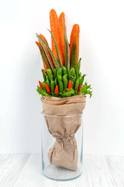 An original vegetable bouquet consisting of carrots, pea pods, lettuce leaves, red pepper and aloe is stand in a glass vase