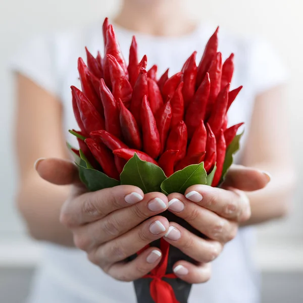 Girl gives a small bouquet made of red hot peppers in the form of a heart