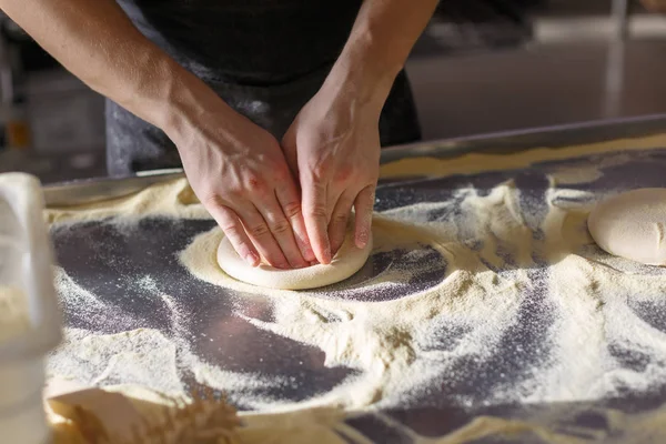 Baker kneads dough for pizza in the kitchen in the restaurant