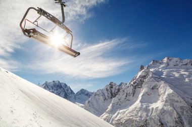 Arka plan mavi gökyüzü, karla kaplı dağlar ve parlak kış güneşi üzerinde bir dağın üzerinde sandalye Asansör