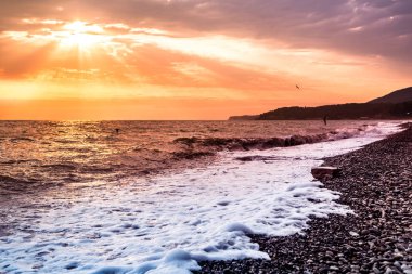 Denizin kenarında rüzgarlı havalarda mistik turuncu-kırmızı günbatımı