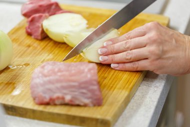 Kadın bir ahşap tahta üzerine soğan ve çiğ et keser