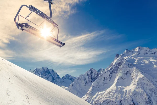 在蓝天 白雪覆盖的山脉和明亮的冬日阳光的背景下 在山腰上举起椅子 — 图库照片