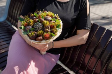 Kadın onun elinde egzotik meyvelerin oluşan buket ile bir bankta oturur