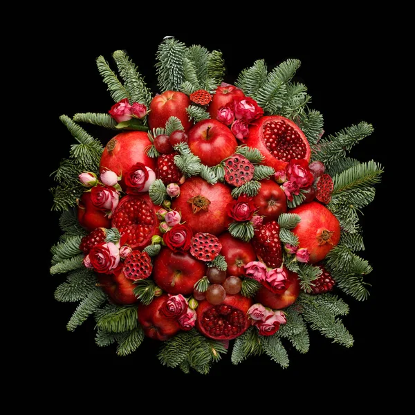 Huge edible fruit bouquet consisting of pomegranates, apples, grapes, rose flowers and fir twigs  on black background. Top view