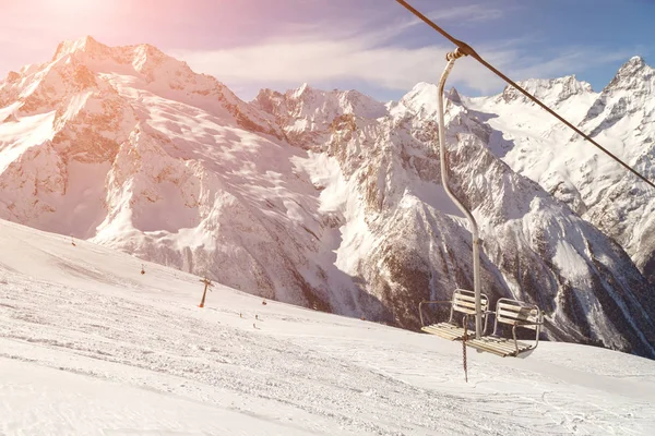 在阳光明媚的冬日 高加索山脉山脊背景上的双椅滑雪缆车 — 图库照片