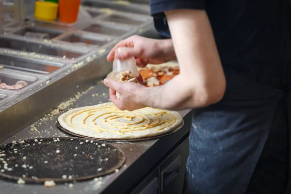 Baker lays chicken meat on the pizza base spread by mayonnaise