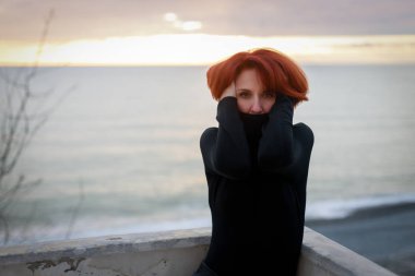 Kırmızı saçlı ve deniz ve günbatımı arka planda piercing bakmak ile genç bir kadının portresi