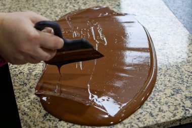 Chocolatier stirs the tempered chocolate on a granite table in order to cool clipart