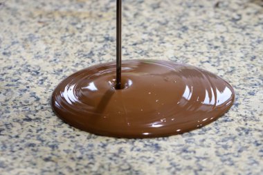Kahverengi önlük içinde Chocolatier granit bir masaya sıvı çikolata döker
