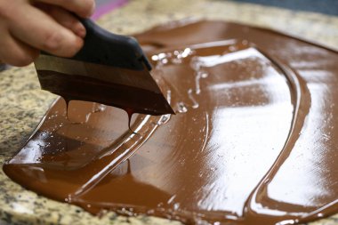 Bir spatula ile Chocolatier bir granit masada temperli sıvı çikolata karıştırıyor