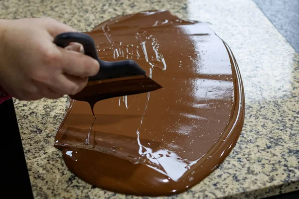 Chocolatier stirs the tempered chocolate on a granite table in order to cool