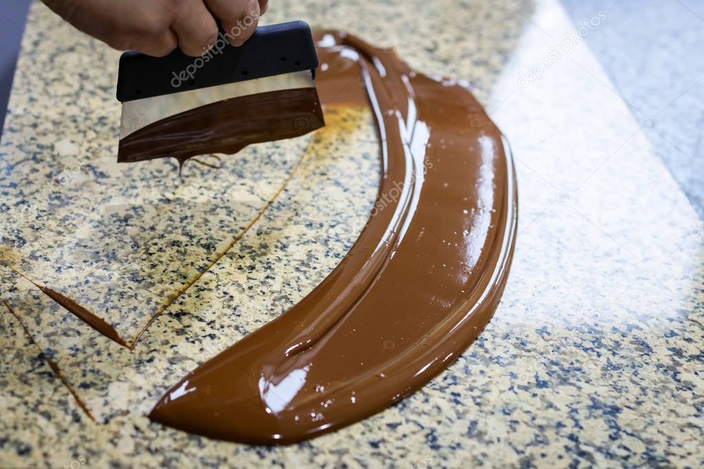 Chocolatier stirs the tempered chocolate on a granite table in order to cool