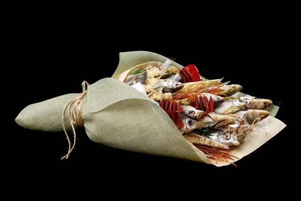 Snacks, dried fish, pistachios packed in the form of a bouquet on a black background. Side view