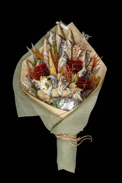 Snacks, dried fish, pistachios packed in the form of a bouquet on a black background. Top view