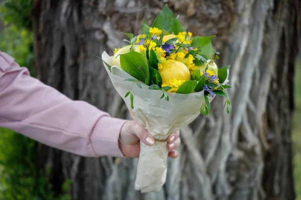 Young woman gives a bouquet of yellow and blue flowers and fruits