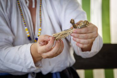 Rus etnik kıyafetli kadın samandan küçük bir oyuncak yapıyor.