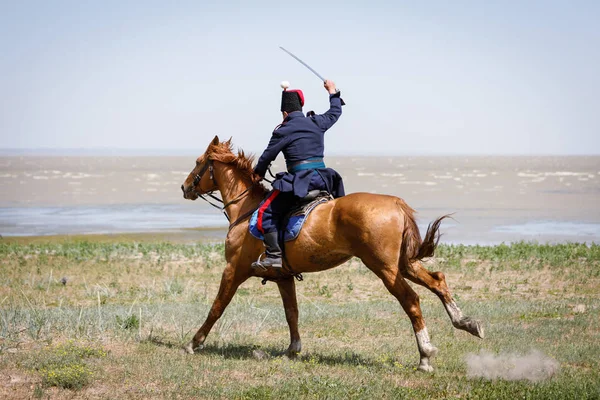 Horseman in blue military clothes riding along the seashore with a sabre in his hand