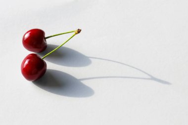 Bir şube üzerinde iki kiraz çilek beyaz bir arka planda güzel bir gölge döküm