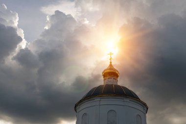 Güneş ışınları, eski kilisenin kubbesindeki altın haçı aydınlatan gök gürültülü bulutların arasından geçiyor.