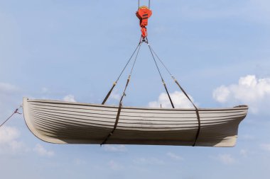 Rowing boat hanging on a crane hook on a blue sky background clipart