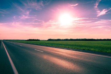 Gün batımında parlak güneşe karşı boş asfalt karayolu. Tonlu görüntü