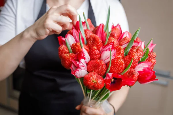 Florist in a black apron corrects position of the flower in the original bouquet of tulips and strawberries