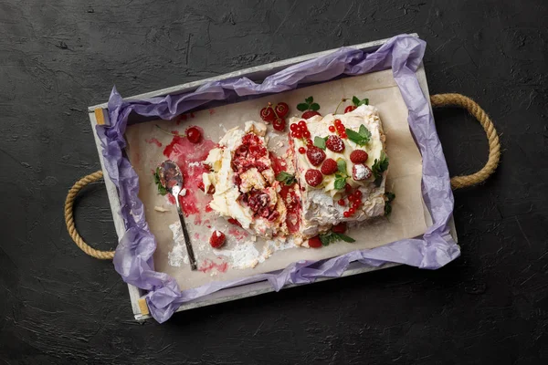 Beautiful meringue roll with fruit lies on a tray on a black background. Top view