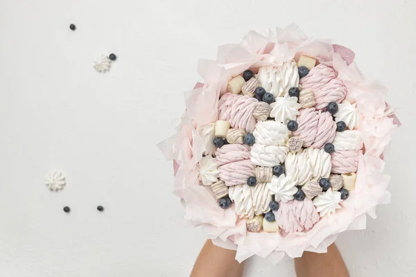 Delicious bouquet consisting of marshmallow, candy and blueberries in male hands on a white background