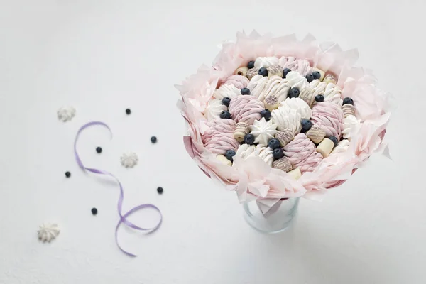 Bouquet of sweets stands in a vase against a background of scattered berries and a purple ribbon