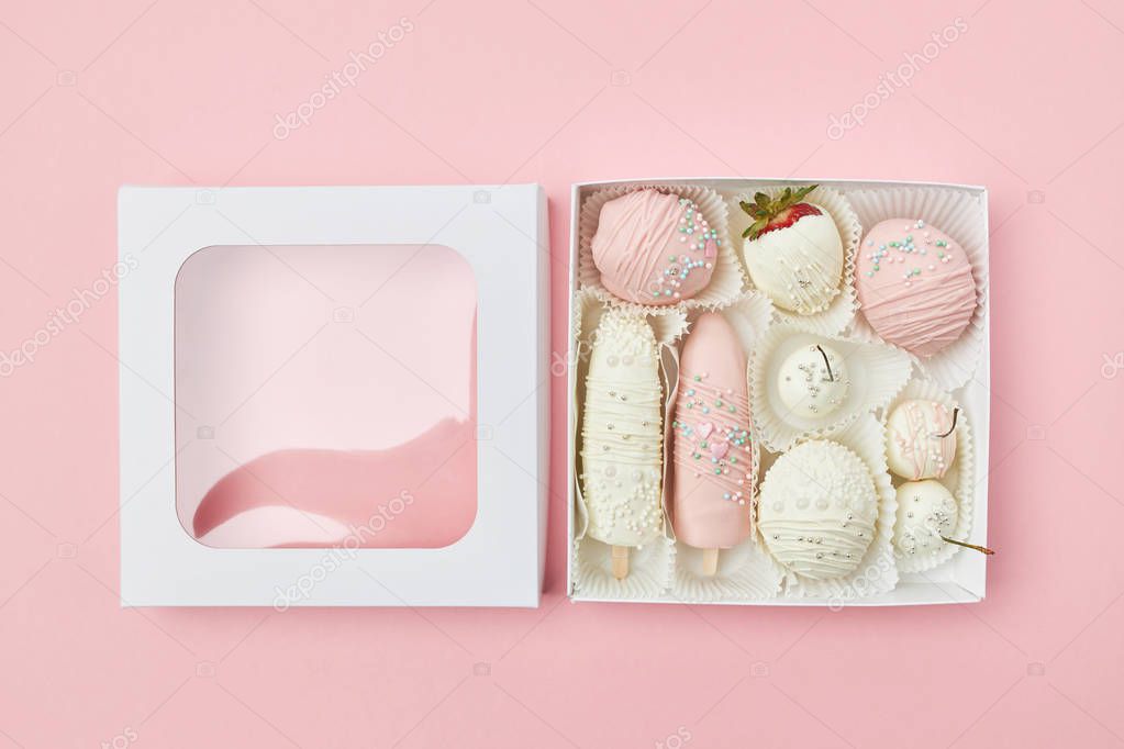 Open gift box with fruits covered in white and pink chocolate are on the pink background