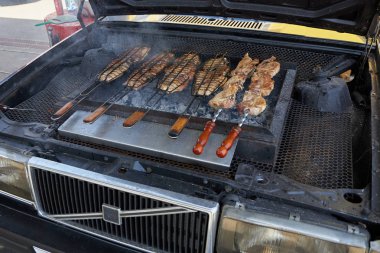ROSTOV-ON-DON, RUSSIA, JUNE 16, 2019: Tasty meat is fried on the grill, made under the hood of an old Volvo car clipart