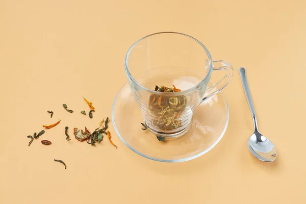 Glass tea cup with spoon and spilled herbal tea on an orange background