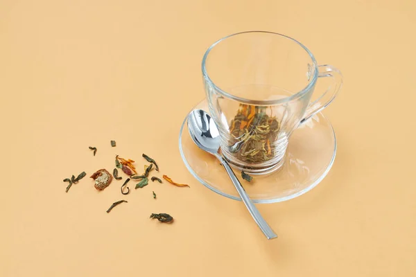 Glass tea cup with spoon and spilled herbal tea on an orange background — Stock Photo, Image