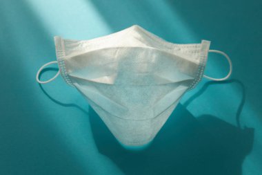 Tıbbi maske, turkuaz bir arka planda güneş ışığında bir yüz şeklinde katlanmış.