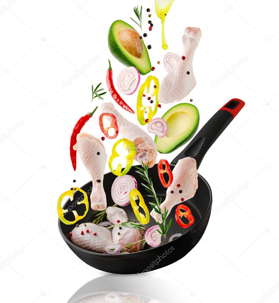 Raw chicken drumsticks and veggies ingredients falling into the frying pan. Isolated on white. Healthy eating