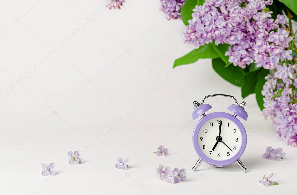 Morning background with lilac flowers and alarm clock. Copy space