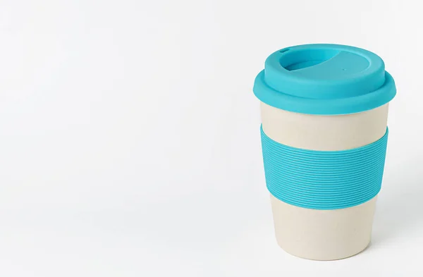 Reusable bamboo coffee cup with blue silicone holder and lid. On white background. Zero waste, copy space