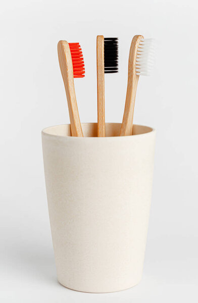 Red, white and black bamboo toothbrushes in eco cup on white background.