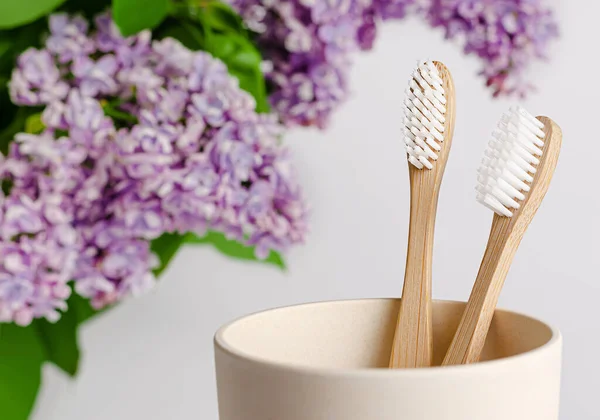 Eco friendly bamboo toothbrush in a cup with lilac flowers on white background.