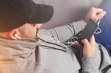 Siyah şapkalı yakışıklı sakallı adamın portresi ya da akıllı telefonlu kulaklıkla müzik dinlemek..