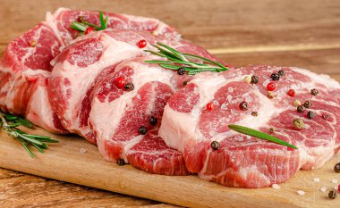 Tahtada çiğ domuz bifteği, karabiber ve ahşap arka planda biberiye. Kapat.