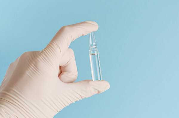 Перчатка, держащая ампулу на синем фоне. Концепция вакцинации

