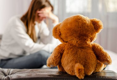 Selected focus on brown teddy bear sitting on depressed and pensive woman background. Infertility and divorce concept clipart