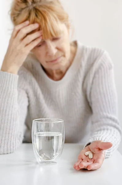 老年妇女手牵着头 有选择地专注于药丸和一杯水 头痛和精神压力的概念 — 图库照片