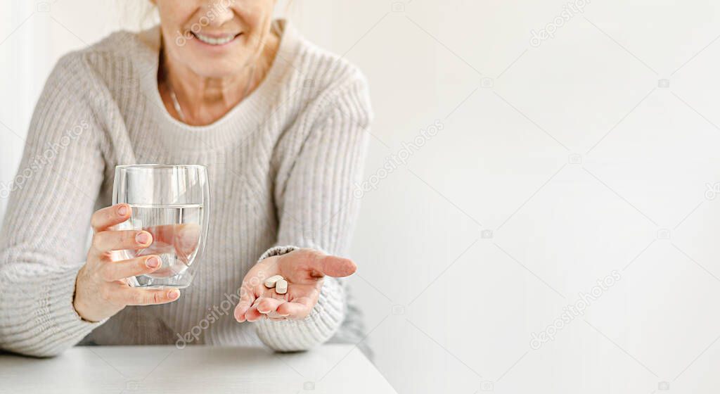 Cropped portrait of smiling elderly woman holding nutritional supplements and a glass of water. Selective focus. Copy space