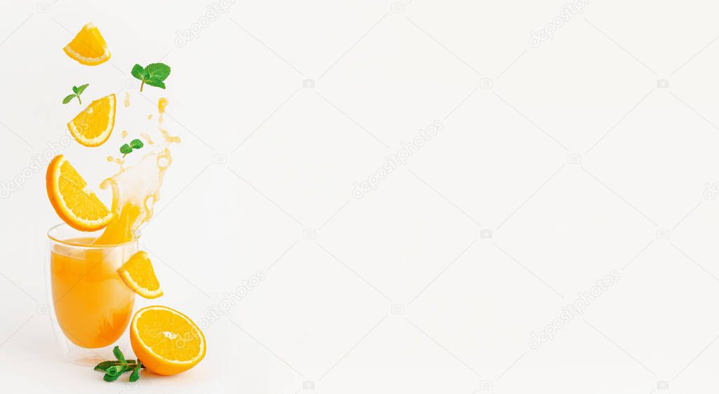 Orange slices and mint flying over the glass of splashing fresh juice. Healthy lifestyle concept.